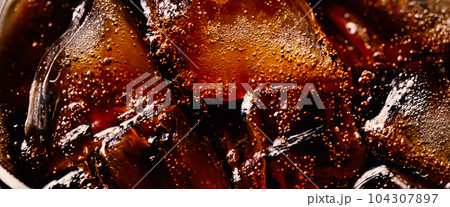 Cola with Ice. Close up of the ice cubes in cola water. Texture of carbonate drink with bubbles in glass. Cola soda and ice splashing fizzing or floating up to top of surface. Cold drink background. Cola with Ice. Close up of the ice cubes in cola water. Texture of carbonate drink with bubbles in glass. Cola soda and ice splashing fizzing or floating up to top of surface. Cold drink background. 104307897