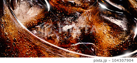 Cola with Ice. Close up of the ice cubes in cola water. Texture of carbonate drink with bubbles in glass. Cola soda and ice splashing fizzing or floating up to top of surface. Cold drink background. 104307904