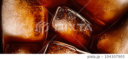 Cola with Ice. Close up of the ice cubes in cola water. Texture of carbonate drink with bubbles in glass. Cola soda and ice splashing fizzing or floating up to top of surface. Cold drink background. Cola with Ice. Close up of the ice cubes in cola water. Texture of carbonate drink with bubbles in glass. Cola soda and ice splashing fizzing or floating up to top of surface. Cold drink background. 104307905