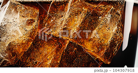 Cola with Ice. Close up of the ice cubes in cola water. Texture of carbonate drink with bubbles in glass. Cola soda and ice splashing fizzing or floating up to top of surface. Cold drink background. Cola with Ice. Close up of the ice cubes in cola water. Texture of carbonate drink with bubbles in glass. Cola soda and ice splashing fizzing or floating up to top of surface. Cold drink background. 104307918
