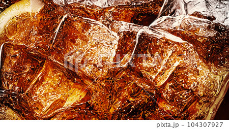 Cola with Ice. Close up of the ice cubes in cola water. Texture of carbonate drink with bubbles in glass. Cola soda and ice splashing fizzing or floating up to top of surface. Cold drink background. Cola with Ice. Close up of the ice cubes in cola water. Texture of carbonate drink with bubbles in glass. Cola soda and ice splashing fizzing or floating up to top of surface. Cold drink background. 104307927