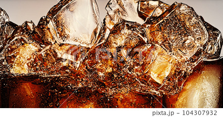 Cola with Ice. Close up of the ice cubes in cola water. Texture of carbonate drink with bubbles in glass. Cola soda and ice splashing fizzing or floating up to top of surface. Cold drink background. Cola with Ice. Close up of the ice cubes in cola water. Texture of carbonate drink with bubbles in glass. Cola soda and ice splashing fizzing or floating up to top of surface. Cold drink background. 104307932