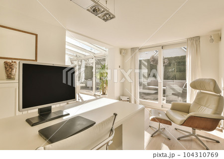 a living room with a flat screen tv on the wall and an office chair next to it in front of a large window a living room with a flat screen tv on the wall and an office chair next to it in front of a large window 104310769
