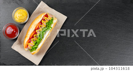 Homemade Hot Dog with mustard, ketchup, tomato and fresh salad leaves on black slate background Homemade Hot Dog with mustard, ketchup, tomato and fresh salad leaves on black slate background 104311618