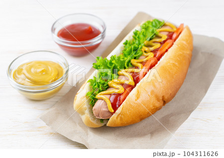 Homemade Hot Dog with mustard, ketchup, tomato and fresh salad leaves on white wooden background Homemade Hot Dog with mustard, ketchup, tomato and fresh salad leaves on white wooden background 104311626