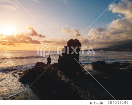 young man standing on rock or cliff on ocean shore at sunset, aerial view young man standing on rock or cliff on ocean shore at sunset, aerial view 104312142
