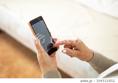 Close up of the hands from middle aged woman sitting on sofa at home and using her mobile phone. 104312852