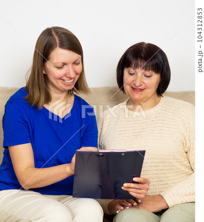 Young caregiver showing a precsription or document and helping senior woman at home. 104312853