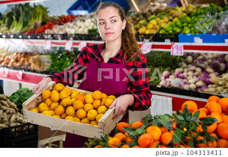 Young smiling woman salesman carrying box with yellow plums 104313411