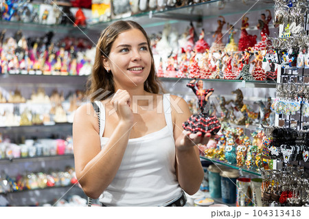 Cheerful girl choosing ceramic figurines of flamenco dancers in souvenir shop 104313418
