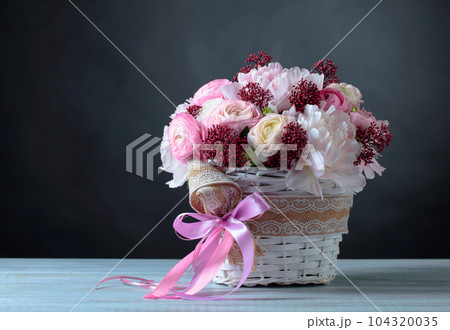 Bouquet of pink peonies in white basket with pink ribbon. 104320035