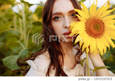 Portrait of a young woman with a sunflower near her face 104320503