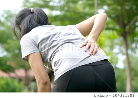Woman's hand She is caught at the waist and her back is painful at the back in the park. Cause of the exercise. Woman's hand She is caught at the waist and her back is painful at the back in the park. Cause of the exercise. 104321581