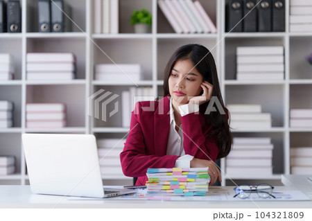 An Asian woman feeling stressed with work, using a laptop to create a report for a finance company. Depicting accounting and financial concepts An Asian woman feeling stressed with work, using a laptop to create a report for a finance company. Depicting accounting and financial concepts 104321809
