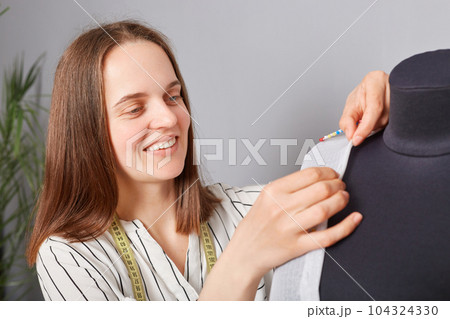 Closeup of cheerful woman sewer sewing dress or shirt in atelier working process in tailoring workshop creating new stylish trendy attire. Closeup of cheerful woman sewer sewing dress or shirt in atelier working process in tailoring workshop creating new stylish trendy attire. 104324330