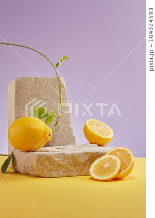 Minimalist abstract background for cosmetic presentation with lemon ingredient. Gray block of stone, lemon and lemon slices with vines decorated on purple. Front view. Concept for natural extract 104324593