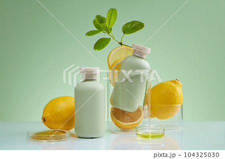 Creative layout with two bottles arranged with glassware, lemon and petri dishes filled with yellow fluid. Natural beauty blank label for branding mock-up concept 104325030