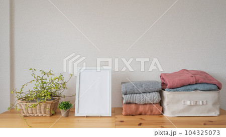 たたまれた冬物の服と白いフレーム｜洗濯物・衣替えイメージ 104325073