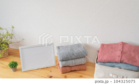 たたまれた冬物の服と白いフレーム｜洗濯物・衣替えイメージ 104325075