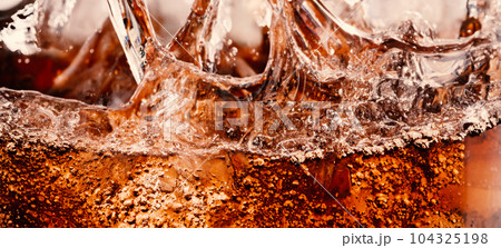 Splashing of Cola and Ice. Cola soda and ice splashing fizzing or floating up to top of surface. Close up of ice in cola water. Texture of carbonate drink with bubbles in glass. Cold drink background Splashing of Cola and Ice. Cola soda and ice splashing fizzing or floating up to top of surface. Close up of ice in cola water. Texture of carbonate drink with bubbles in glass. Cold drink background 104325198