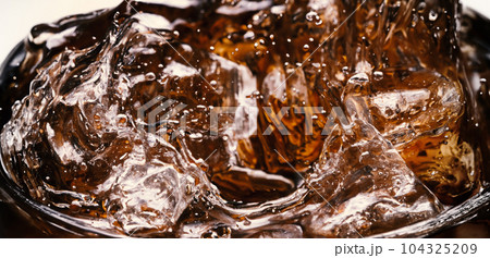 Splashing of Cola and Ice. Cola soda and ice splashing fizzing or floating up to top of surface. Close up of ice in cola water. Texture of carbonate drink with bubbles in glass. Cold drink background Splashing of Cola and Ice. Cola soda and ice splashing fizzing or floating up to top of surface. Close up of ice in cola water. Texture of carbonate drink with bubbles in glass. Cold drink background 104325209