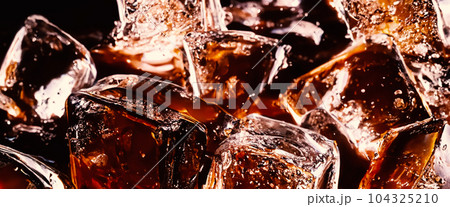 Splashing of Cola and Ice. Cola soda and ice splashing fizzing or floating up to top of surface. Close up of ice in cola water. Texture of carbonate drink with bubbles in glass. Cold drink background Splashing of Cola and Ice. Cola soda and ice splashing fizzing or floating up to top of surface. Close up of ice in cola water. Texture of carbonate drink with bubbles in glass. Cold drink background 104325210