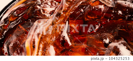 Splashing of Cola and Ice. Cola soda and ice splashing fizzing or floating up to top of surface. Close up of ice in cola water. Texture of carbonate drink with bubbles in glass. Cold drink background Splashing of Cola and Ice. Cola soda and ice splashing fizzing or floating up to top of surface. Close up of ice in cola water. Texture of carbonate drink with bubbles in glass. Cold drink background 104325253