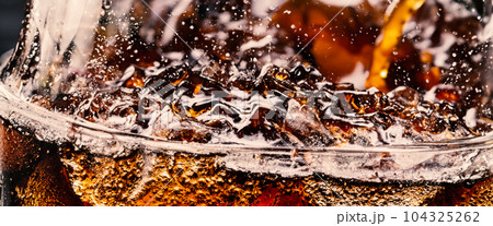 Splashing of Cola and Ice. Cola soda and ice splashing fizzing or floating up to top of surface. Close up of ice in cola water. Texture of carbonate drink with bubbles in glass. Cold drink background Splashing of Cola and Ice. Cola soda and ice splashing fizzing or floating up to top of surface. Close up of ice in cola water. Texture of carbonate drink with bubbles in glass. Cold drink background 104325262