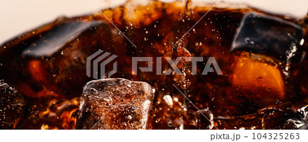 Splashing of Cola and Ice. Cola soda and ice splashing fizzing or floating up to top of surface. Close up of ice in cola water. Texture of carbonate drink with bubbles in glass. Cold drink background Splashing of Cola and Ice. Cola soda and ice splashing fizzing or floating up to top of surface. Close up of ice in cola water. Texture of carbonate drink with bubbles in glass. Cold drink background 104325263