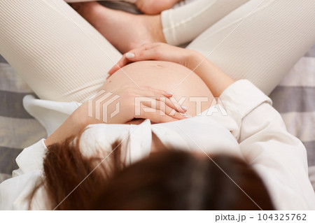 Pregnancy, love, healthcare, motherhood, people, relaxation and expectation. Young beautiful pregnant woman sitting holding her belly in top view. 104325762
