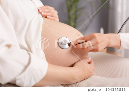 Anonymous faceless pregnant woman sitting in clinic doctor using stethoscope, female with bare belly taking care of her health vising clinic. 104325811