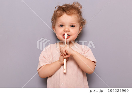 Adorable infant little girl holding toothbrush isolated on gray background brushing her teeth with tiny toothbrush looking at camera children oral care. 104325960