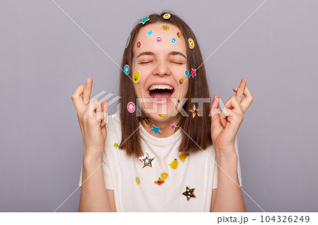 Hopeful woman with fingers crossed. Young female crossing fingers on both hands, laughing and screwing up eyes, praying for good luck, dreaming, making wish. Hopeful woman with fingers crossed. Young female crossing fingers on both hands, laughing and screwing up eyes, praying for good luck, dreaming, making wish. 104326249