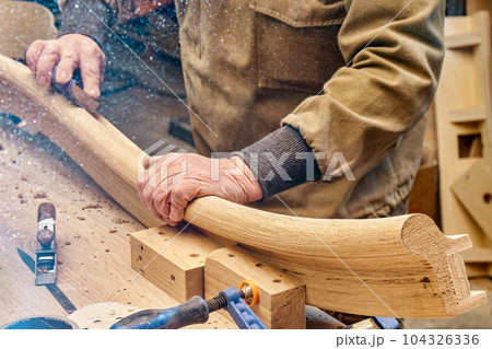 Carpenter sands bending wooden railing with sandpaper in workshop closeup. Senior master makes detail of spiral staircase for home interior Carpenter sands bending wooden railing with sandpaper in workshop closeup. Senior master makes detail of spiral staircase for home interior 104326336