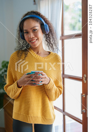African American wearing headphones and holding coffee mugs smiling happily while listening to music relaxing at home African American wearing headphones and holding coffee mugs smiling happily while listening to music relaxing at home 104328287