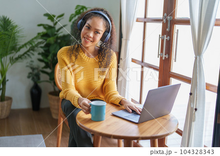 Portrait of an African American wearing headphones holding a coffee cup and using a computer. 104328343