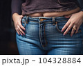 Overweight woman wearing jeans on fat body and blouse demonstrate big hips and belly dark background 104328884