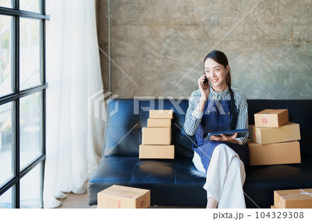 Starting small business entrepreneur of independent Asian female online seller talking on the phone with a customer and packing products for delivery to the customer. and SME delivery concept. Starting small business entrepreneur of independent Asian female online seller talking on the phone with a customer and packing products for delivery to the customer. and SME delivery concept. 104329308