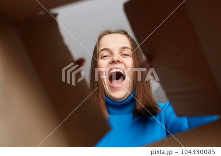 Happy and excited young adult woman looking inside carton box. Looking cheerful and overjoyed, screaming with happiness, good delivery service. View from the bottom of the cardboard box. Happy and excited young adult woman looking inside carton box. Looking cheerful and overjoyed, screaming with happiness, good delivery service. View from the bottom of the cardboard box. 104330085