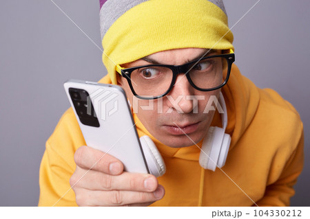 Closeup shot of funny attentive man gazes with surprised expression at mobile phone display wears casual closing isolated over gray background looks with big interest at smart phone. Closeup shot of funny attentive man gazes with surprised expression at mobile phone display wears casual closing isolated over gray background looks with big interest at smart phone. 104330212