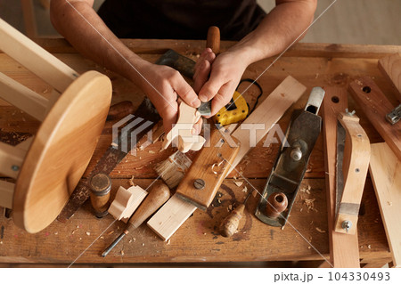 Closeup shot of unrecognizable faceless man carpenter making a handmade wooden toy in a home workshop, working on table among carpentry tools, wood carving. 104330493