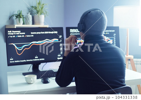 Back view of businessman or programmer in gray cap sitting at desk in office with multiple screens, looking at the graphs, exchange and money, investment data on cryptocurrency stock market chart. 104331338