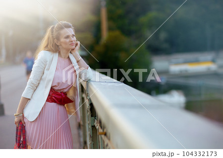 pensive elegant woman in pink dress and white jacket in city 104332173