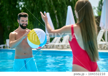 Happy attractive couple having fun in pool with beach ball. 104332210