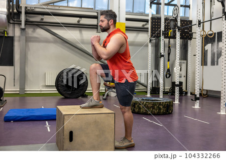 Young strong man doing workout with wooden box step up in crossfit gym. 104332266