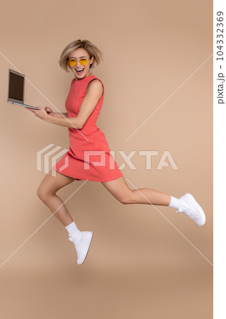 Jumping woman in dress and sunglasses using laptop working online 104332369