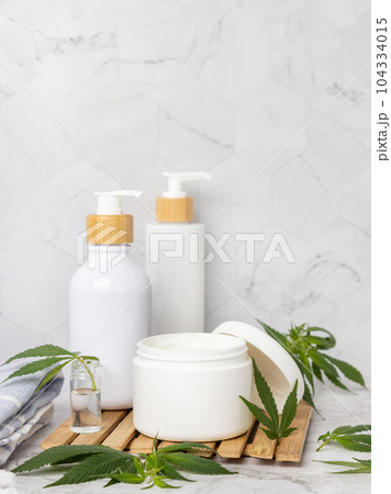 Opened cream jar with blank lid near green cannabis leaves close up, CBD cosmetic mockup 104334015