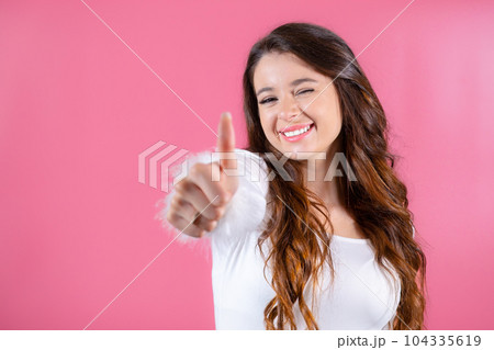 Smiling brunette in white shows like by finger on the pink background.  104335619