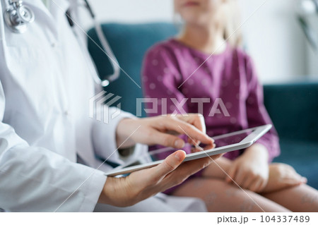 Doctor woman and kid patient at home. The pediatrician uses a tablet computer, close up. Medicine, healthcare concepts 104337489