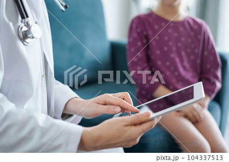 Doctor woman and kid patient at home. The pediatrician uses a tablet computer, close up. Medicine, healthcare concepts 104337513